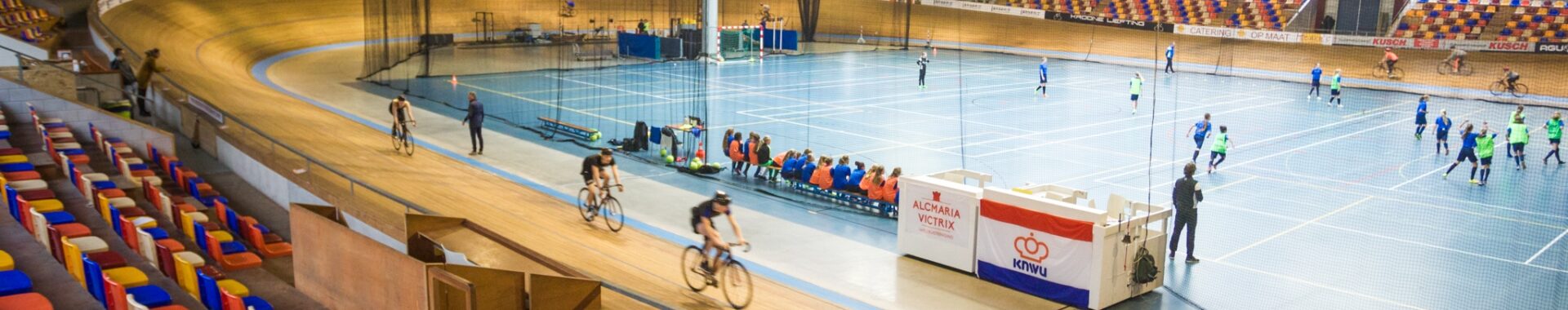 Tribune, wielerbaan met renners en sportvloer met sporters